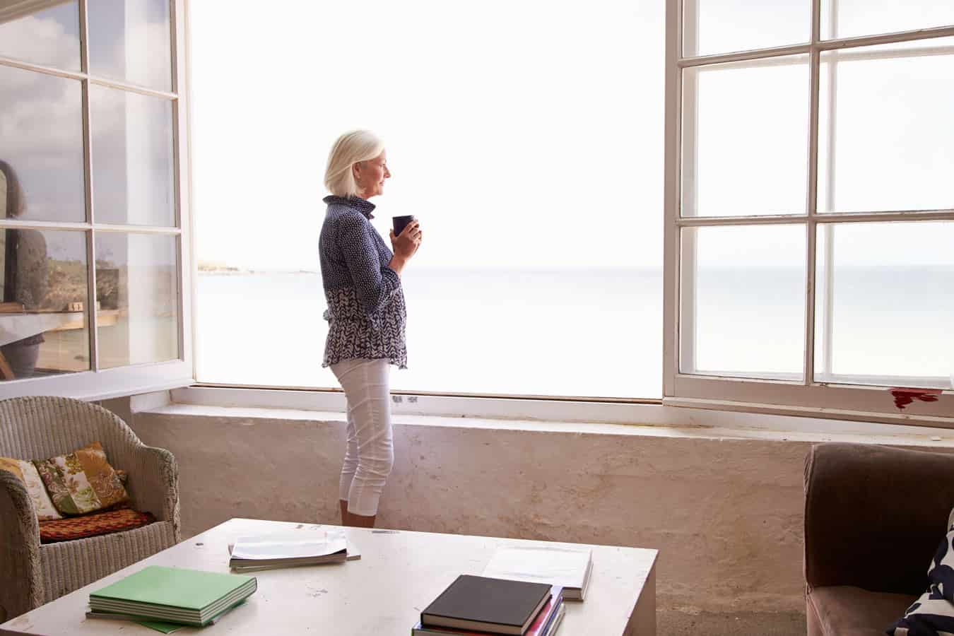 timeshare-owner-wont-admit-her-purchase-was-a-mistake-while-she-looks-out-the-resort-window-with-a-coffee-in-her-hand