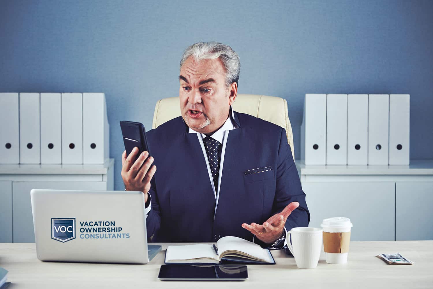 older-man-rich-well-dressed-on-phone-looking-confused-while-in-blue-office-speaking-to-legal-team-about-bankruptcy-claim-and-inability-to-get-rid-of-timeshare-properties