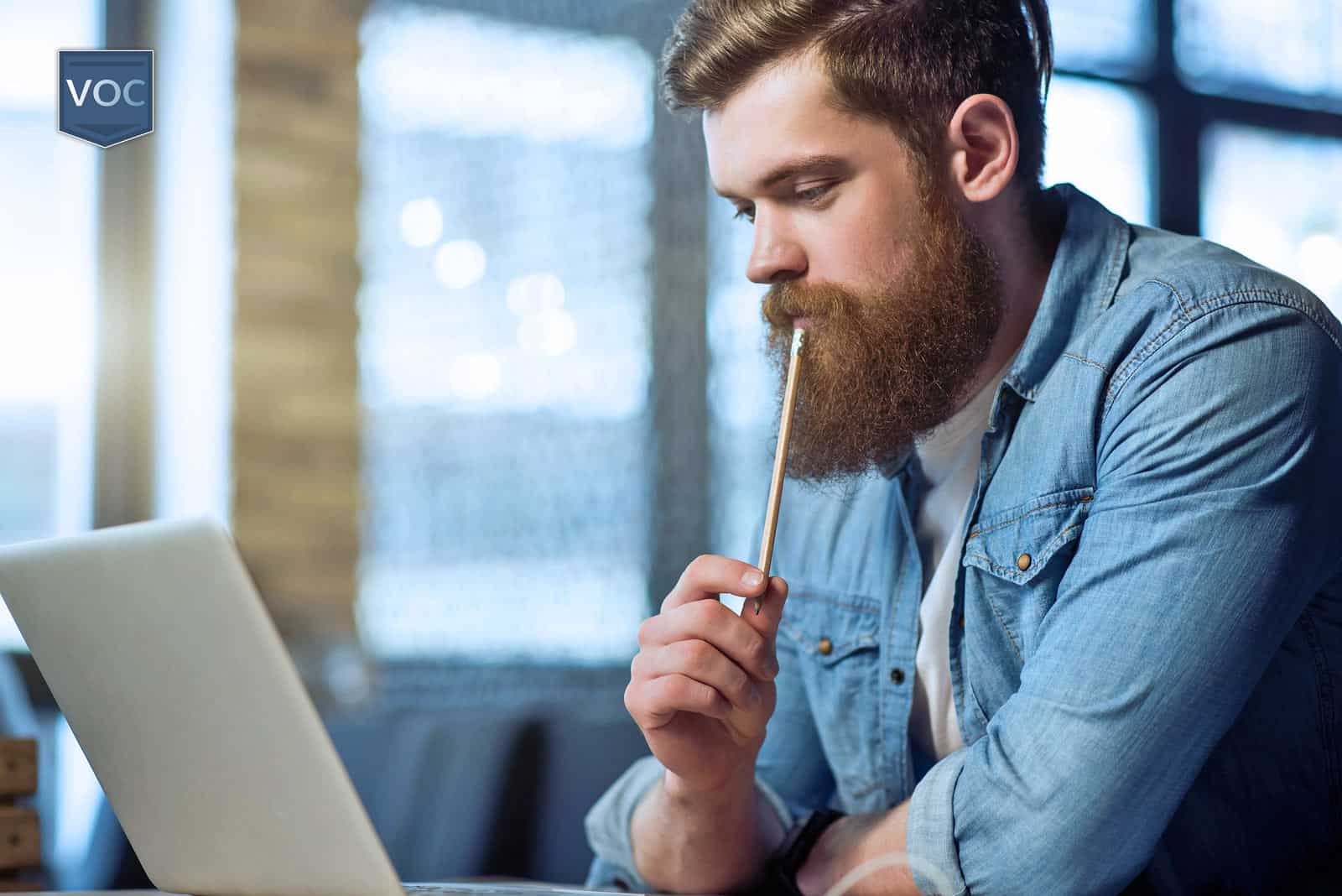 man-committed-to-finding-resolve-online-while-reading-important-details-in-computer-screen-as-he-thinks-through-his-exit-options-with-pencil-before-making-decision