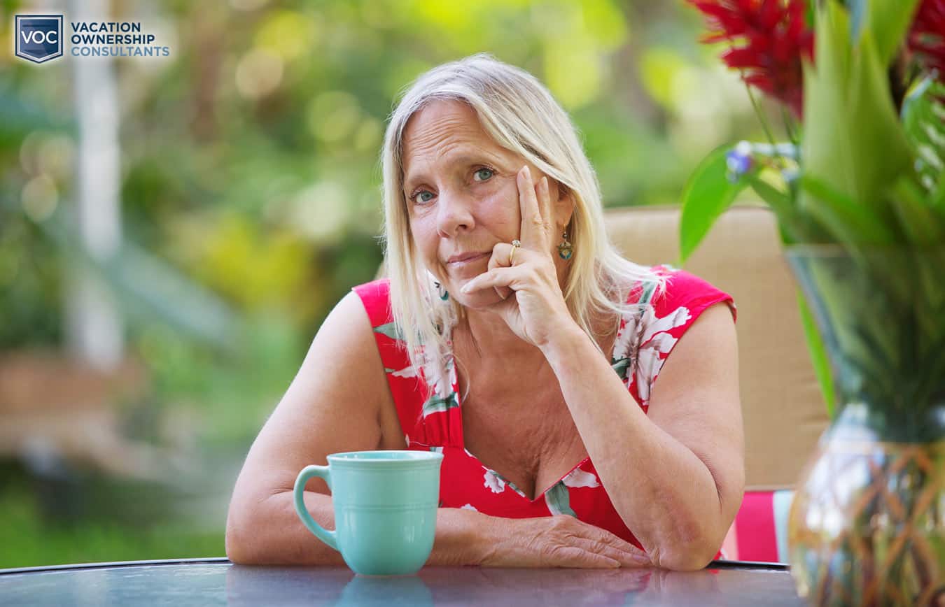 lady-looking-upset-while-drinking-coffee-while-on-vacation-at-resort-in-red-flower-dress-alone