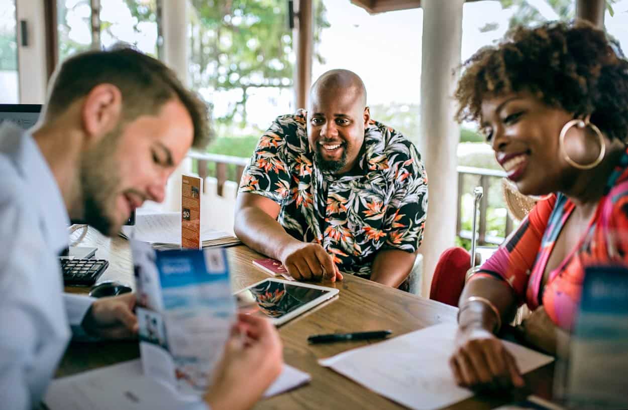 traveling-couple-african-american-middle-age-talking-to-resort-salesman-about-timeshare-upgrades-upon-arrival-to-family-vacation