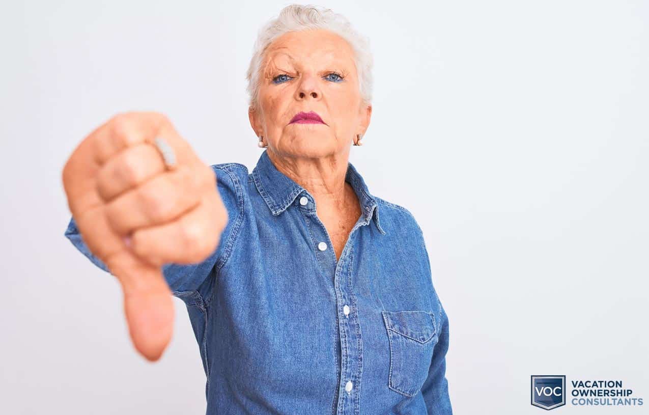 older-woman-makeup-blue-demin-shirt-thumbs-down-to-getting-sick-in-isolated-location-for-now