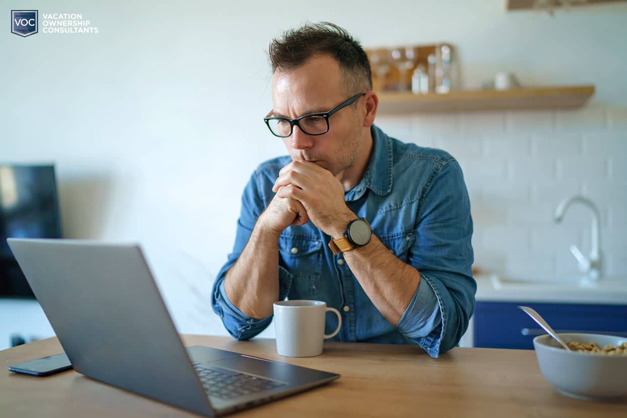 glasses-denim-button-up-man-thinking-at-computer-about-timeshare-relief-program-that's-actually-lead-generation-site