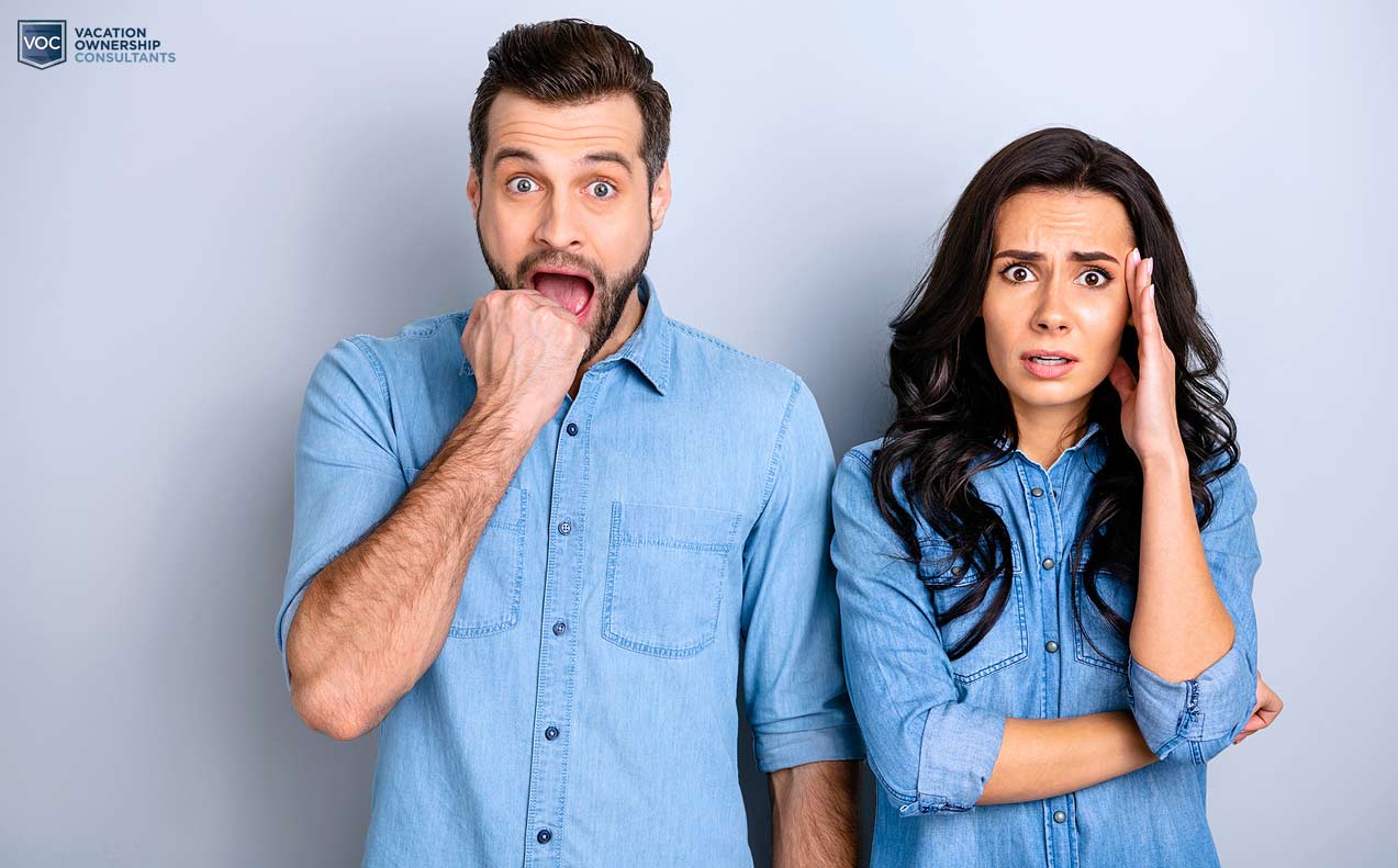 man-and-woman-on-edge-during-stressful-conversation-about-timeshare-mortgage-cancellation-options-for-vacation-owners-denim-shirts-grey-backdrop