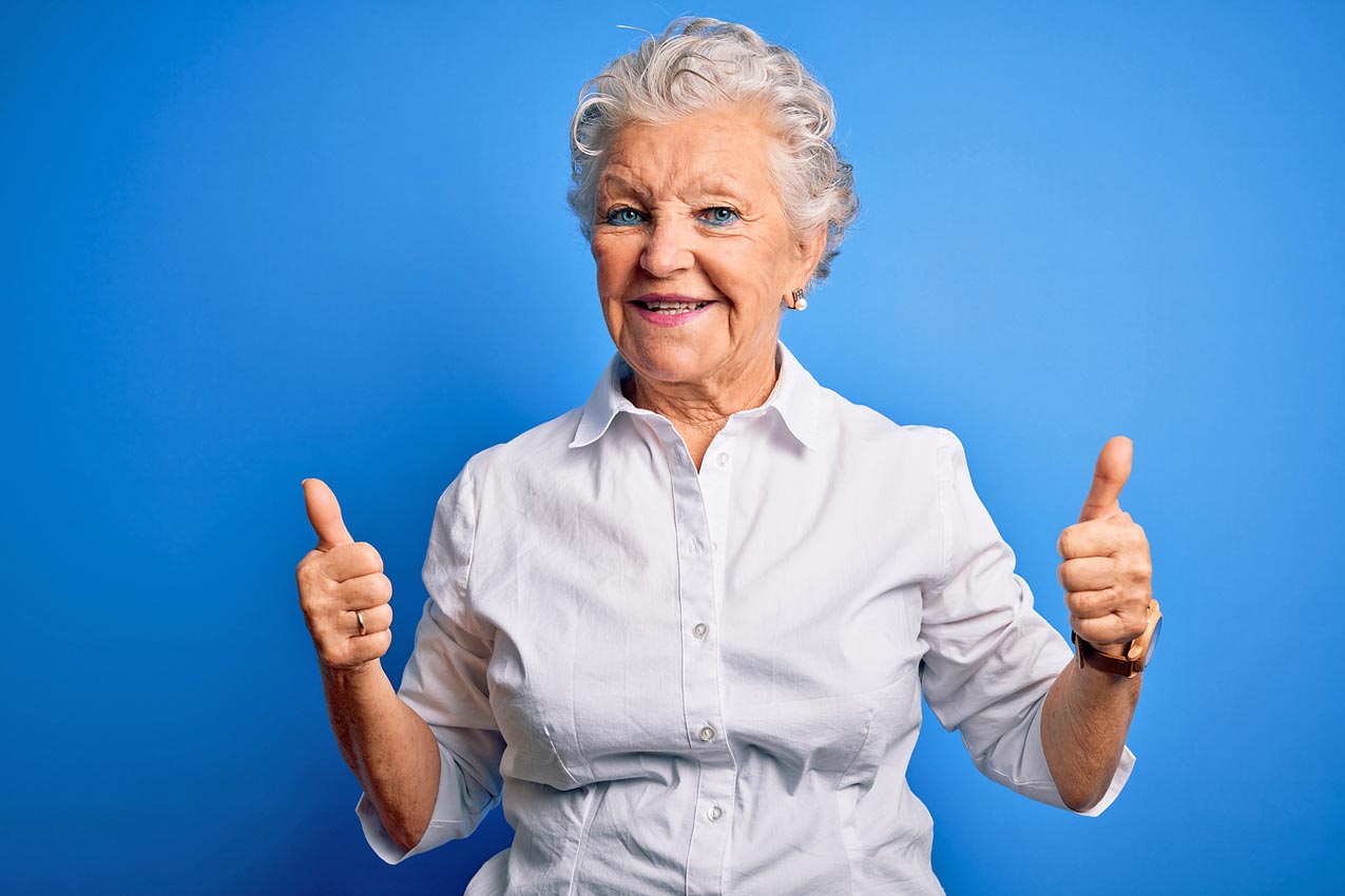 thumbs-up-by-gma-who-is-happy-with-timeshare-vacation-package-after-reviewing-all-contract-terms-blue-background-white-blouse-all-smiles