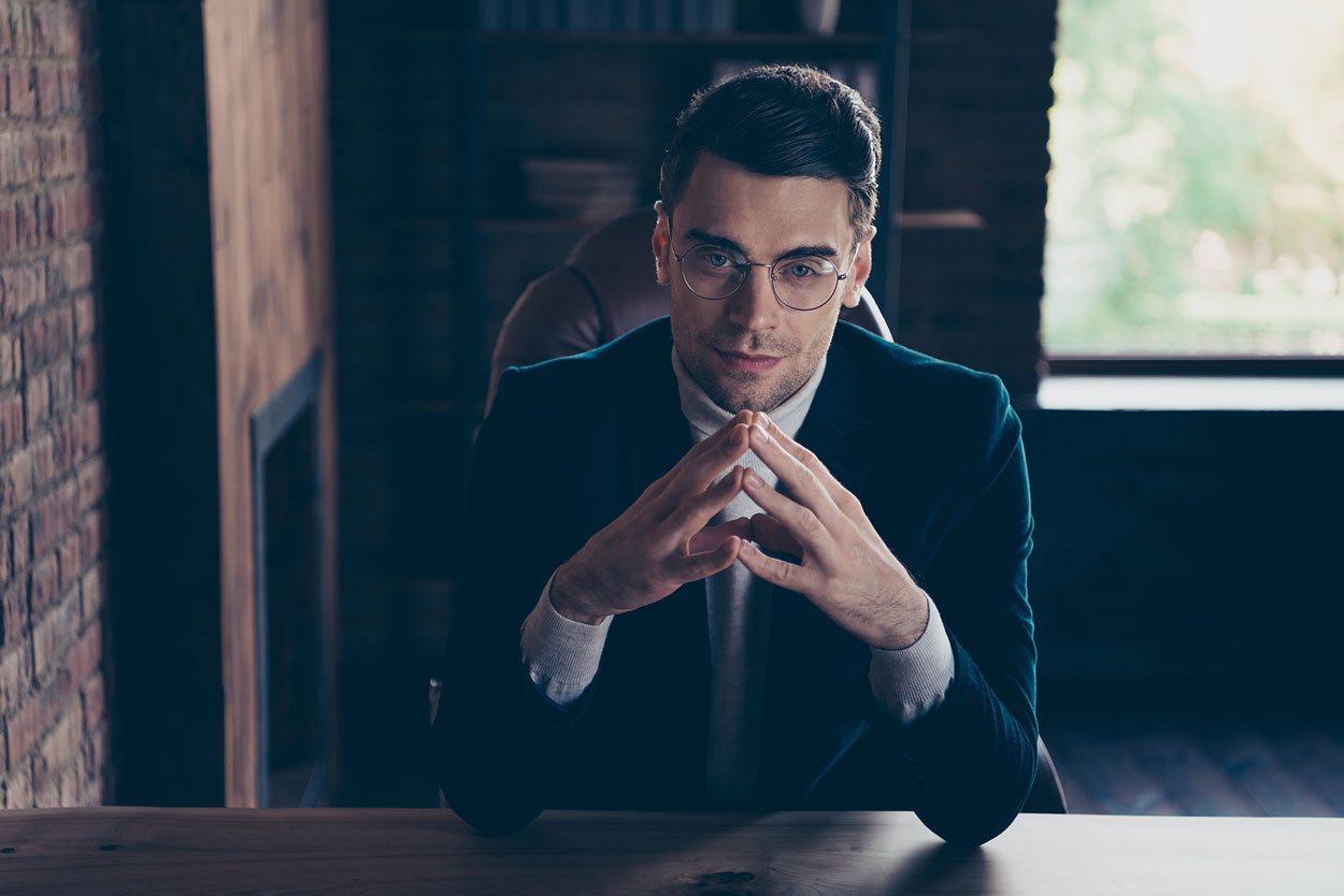 creepy-looking-vacation-salesman-folded-hands-in-dark-room-shadows-to-portray-inescapable-situation-or-scenario